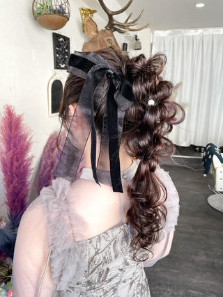 編み下ろし＋ポニーのMIXヘア。立体感のあるルーズな編み込みで華やかなヘアアレンジ。程よく引き出した毛束が柔らかさと動きを演出し、バックスタイルまで抜かりなく印象的に仕上げています。ブラックのシアーリボンとパールアクセサリーを添えることで、甘さの中に大人っぽさと上品さをプラス。結婚式やパーティーなど、特別な一日にぴったりな一線を画すスタイルです。 