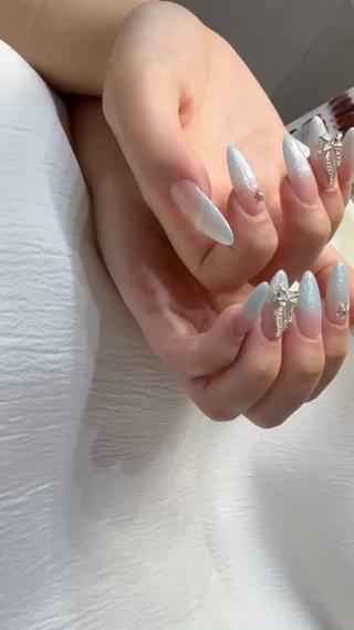 ホワイトグラデ × リボンビジューネイル
透け感のあるホワイト×ブルーのグラデーションに、繊細なラメを重ねた上品なデザイン。
指先をすらっと見せるロングフォルムに、立体リボンとストーンをアクセントに添えて、華やかさと大人の可愛さを両立
清楚で冬らしい透明感があり、ブライダルやイベントにもおすすめです